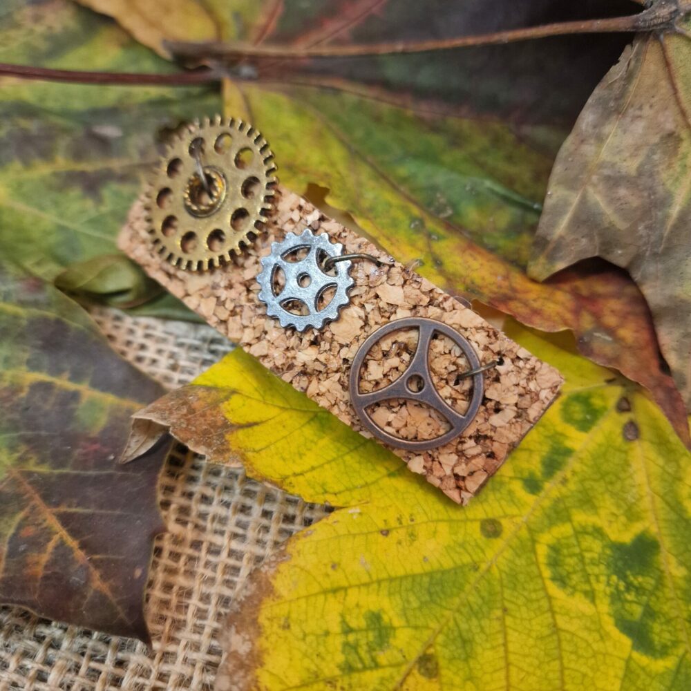 Pince à cheveux artisanale en liège décorée de petits engrenages métalliques dorés et bronze, présentée sur fond de feuilles d’automne.